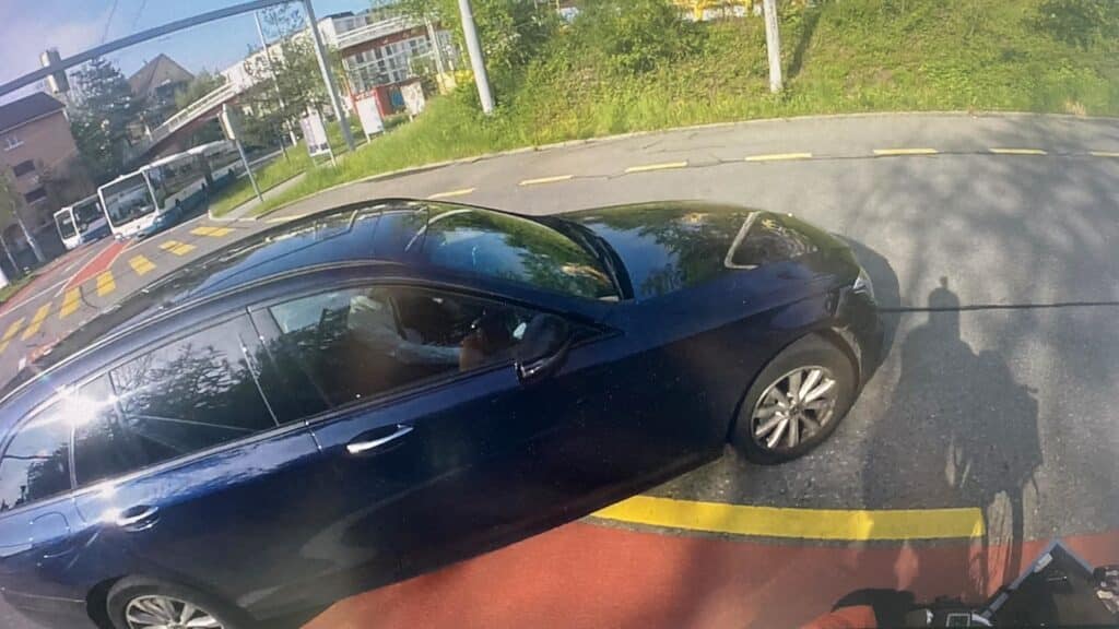 Auf dem Bild sieht man einen Velofahrer auf einer rot markierten Velospur, der von einem Auto abgedrängt wird.