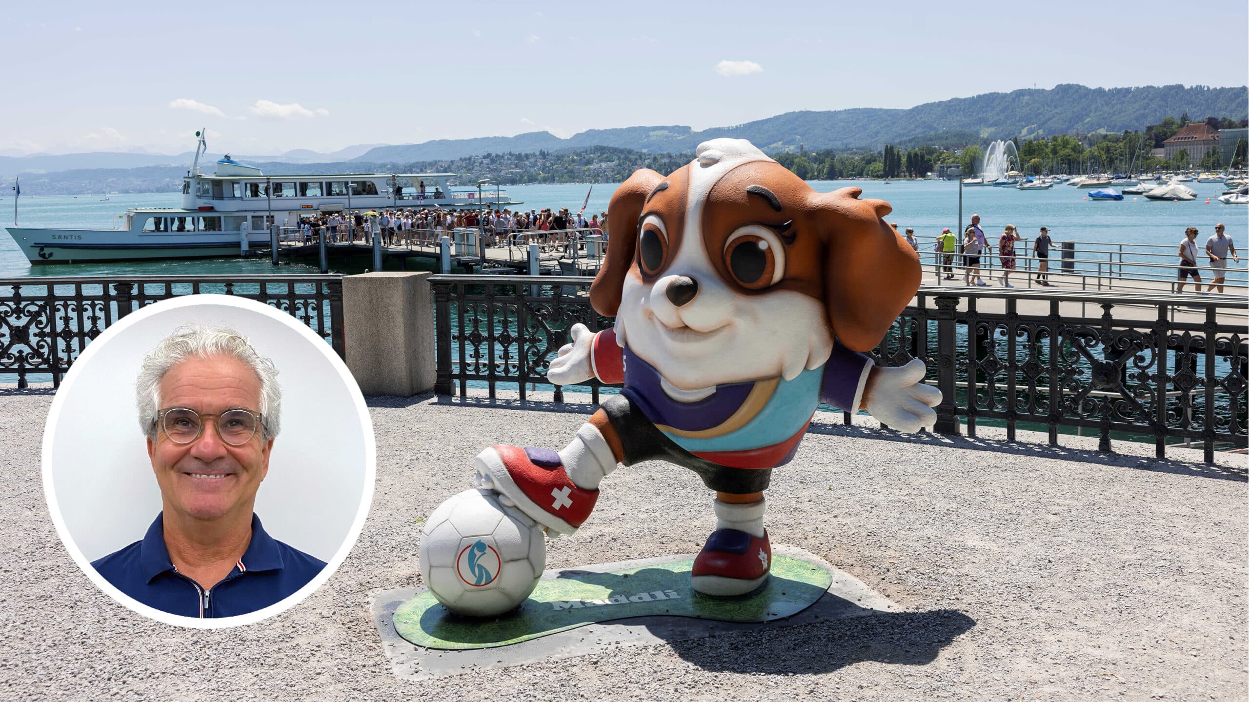 Eine freundlich dreinblickende Figur des Fussball-EM-Maskottchens, ein Bernhardiner-Welpe, steht am Zürcher Seeufer. Das Wetter ist wunderbar und im Hintergrund besteigen Touristinnen und Touristen ein Schiff. Auf dem Bild ist ausserdem mit Photoshop ein Porträtfoto von Lorenz Steinmann auf platziert.