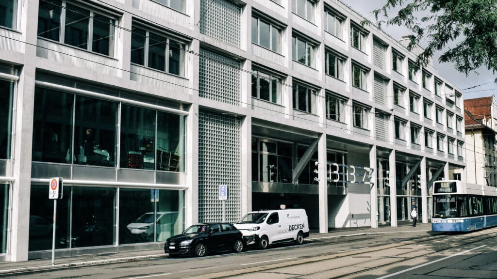 Das Gebäude der BBZ. Davor sind zwei Autos parkiert, ein Flexity-Tram fährt vorbei.