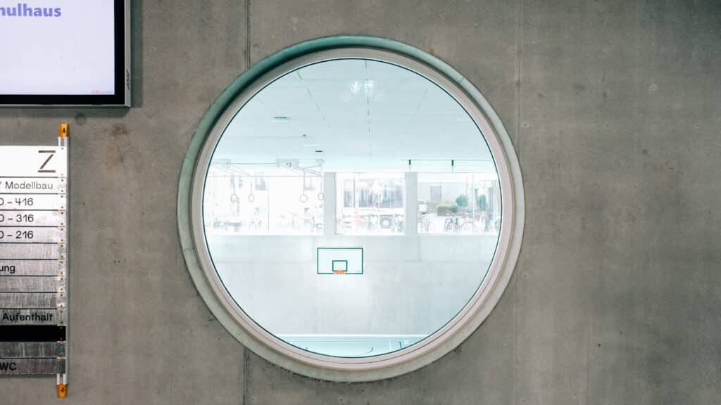 Blick durch ein grosses, rundes Fenster in eine der Sporthallen des Neubaus der BBZ.