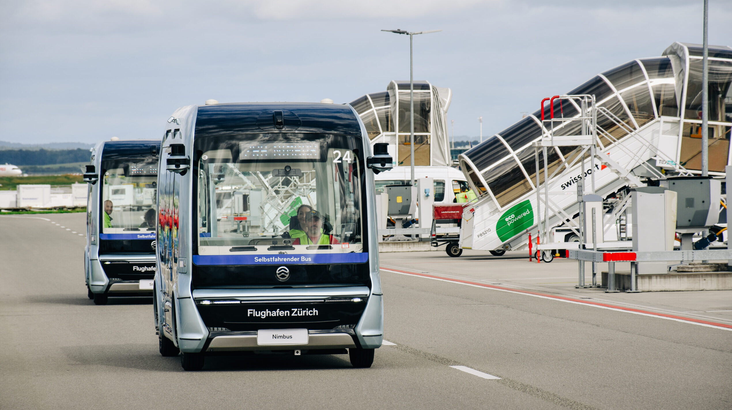 Die zwei Shuttlebusse fahren hintereinander an den Standplätzen am Flughafen vorbei.