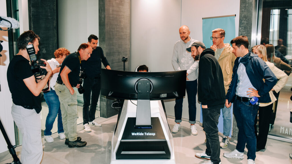 Das Bild zeigt das Remote-Cockpit mit einem riesigen Curved-Bildschirm. Die Medienschaffenden stehen im Halbkreis staunend darum herum.