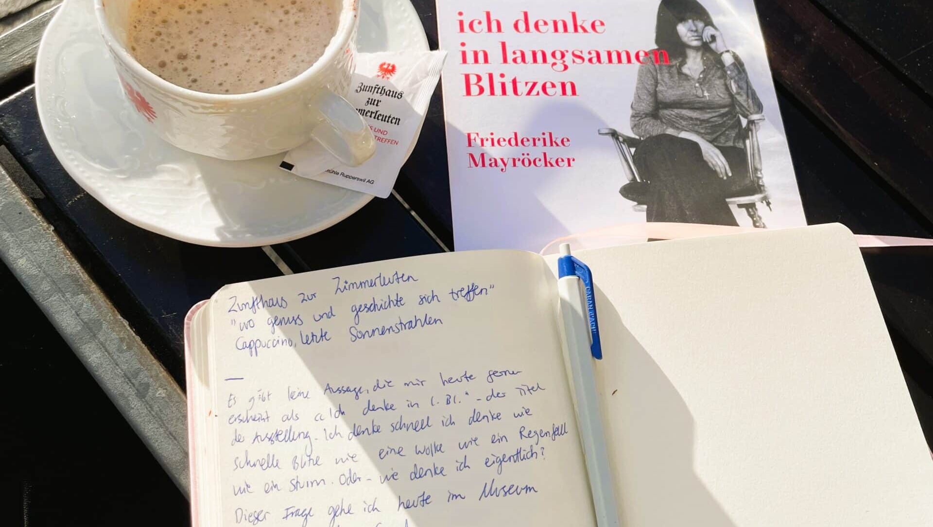 Auf dem Bild sieht man das offene Notizbuch von Lara Hofer neben einer Tasse Kaffee.