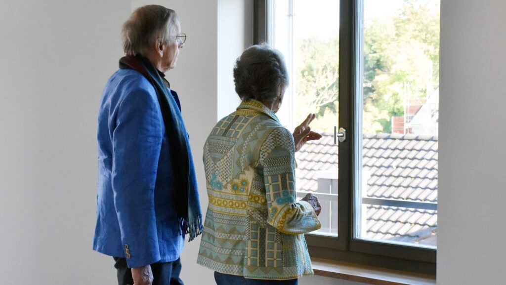 Zwei ältere Personen betrachten den Blick aus dem Fenster einer leeren Stadtwohnung in Zürich.