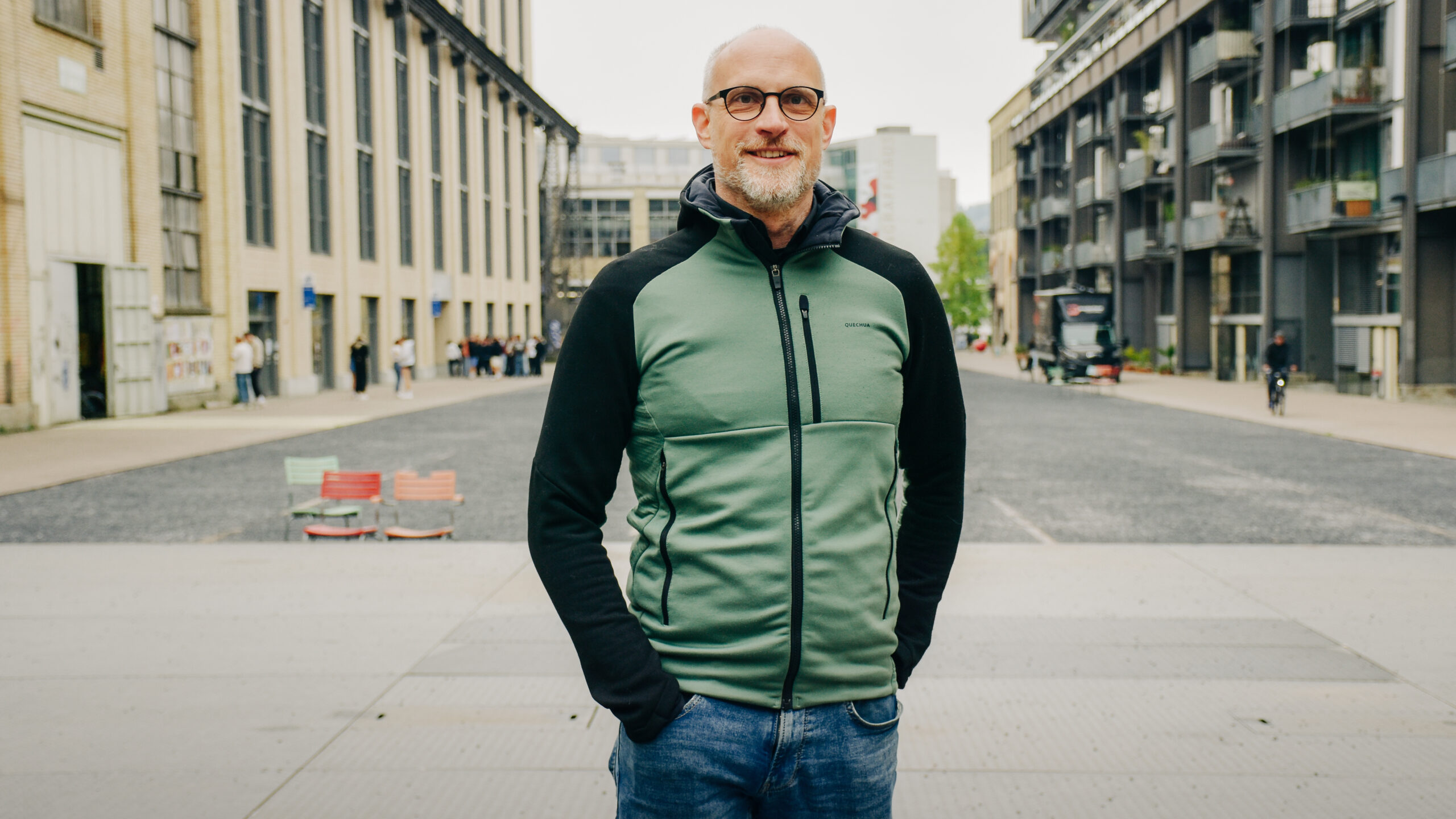 Florian Heer steht auf dem Katharina Sulzer-Platz in Winterthur. Er trägt eine moderne, runde Brille und einen kurzen Bart. Er ist sportlich gekleidet.