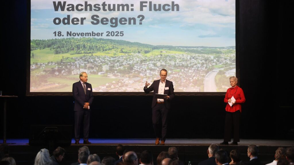 Drei Menschen stehen auf einer Bühne, im Hintergrund eine Leinwand mit dem Schriftzug "Gemeindeforum 2025 – Wachstum: Fluch oder Segen?"