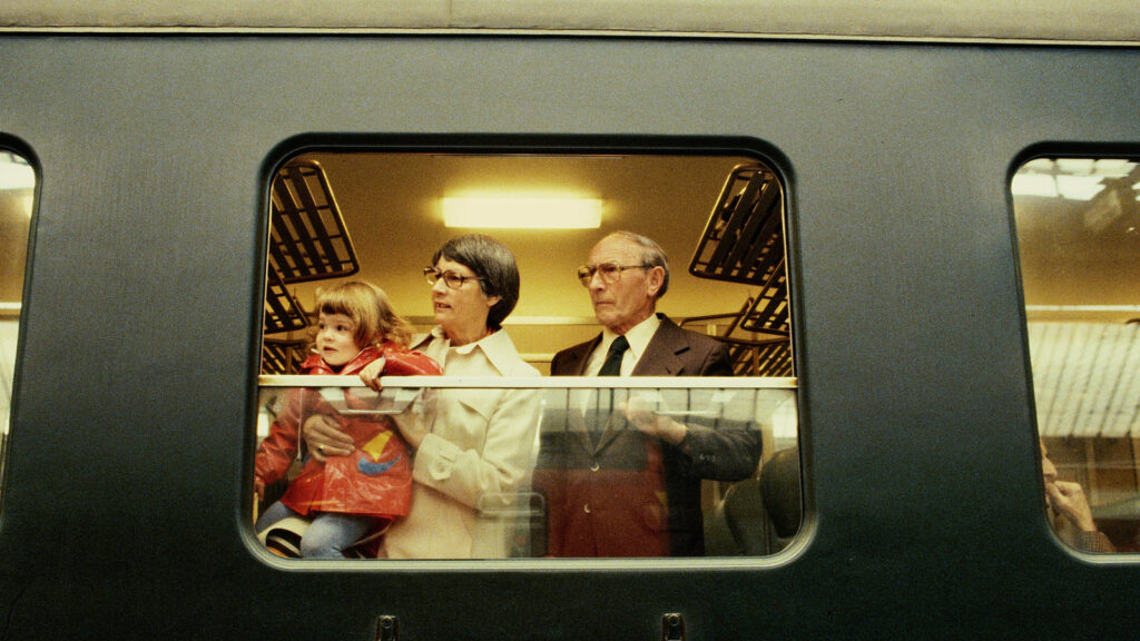 Auf dem Bild sieht man ein älteres Ehepaar mit dem Enkel, wie die drei aus dem Zug schauen.