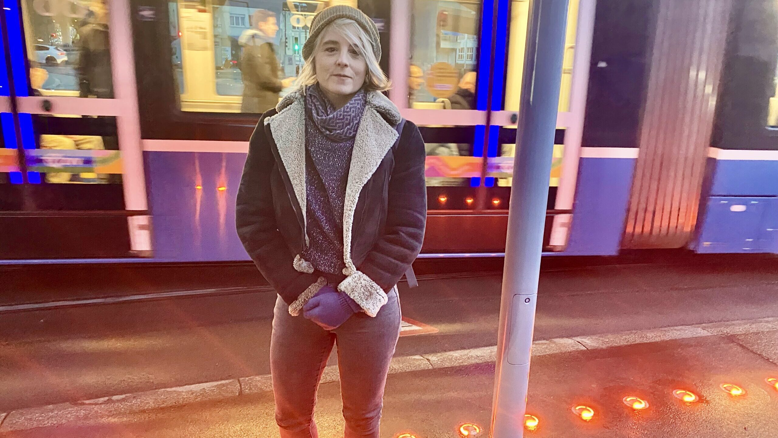 Das Bild zeigt die Politikerin Sandra Bienek auf dem Escher-Wyss-Platz in Zürich. Im Hintergrund ein durchfahrendes Tram, vorne am Boden rote Warnlichter.