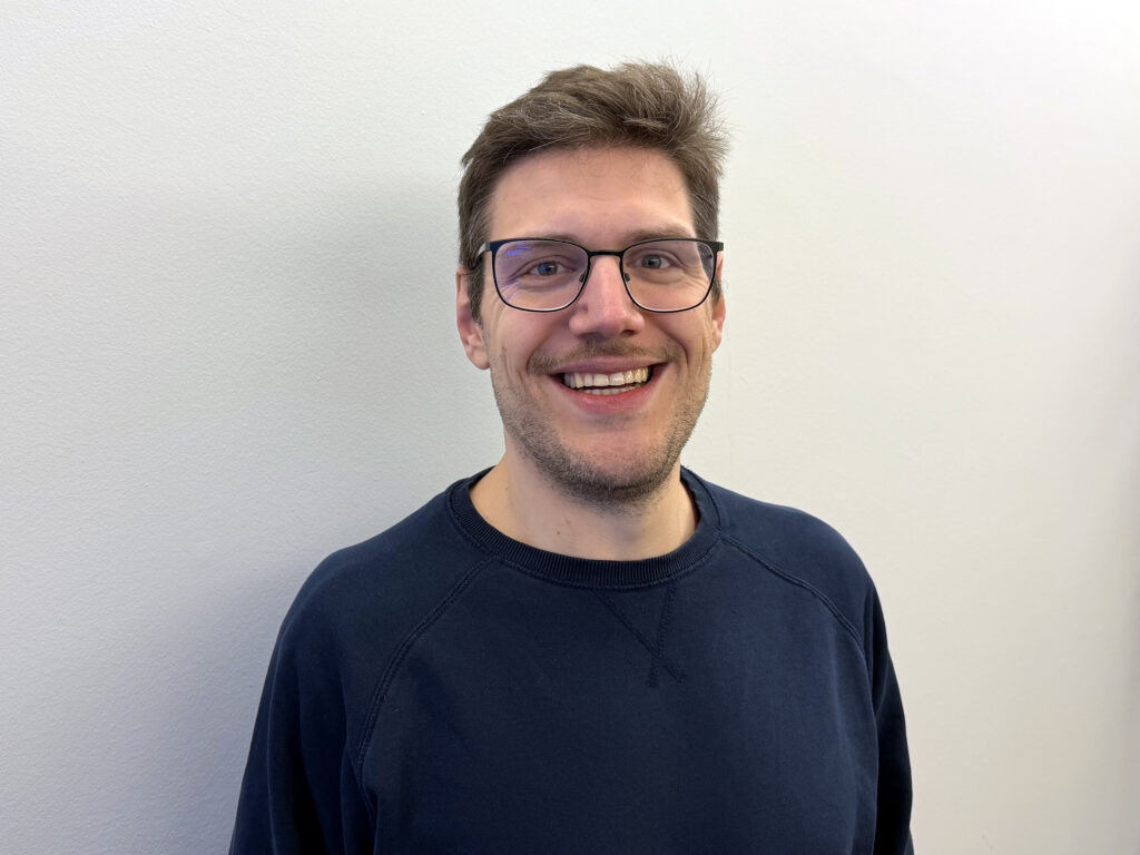 Pascal Turin trägt einen blauen Pullover und eine Brille.