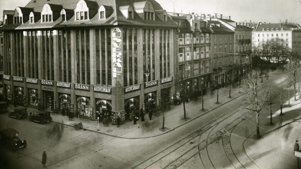 Schwarzweiss Foto eines Warenhausgebäudes an der Bahnhofsstrasse in Zürich. Auf der Strasse stehen Autos aus der Zeit der 1920er-Jahre.