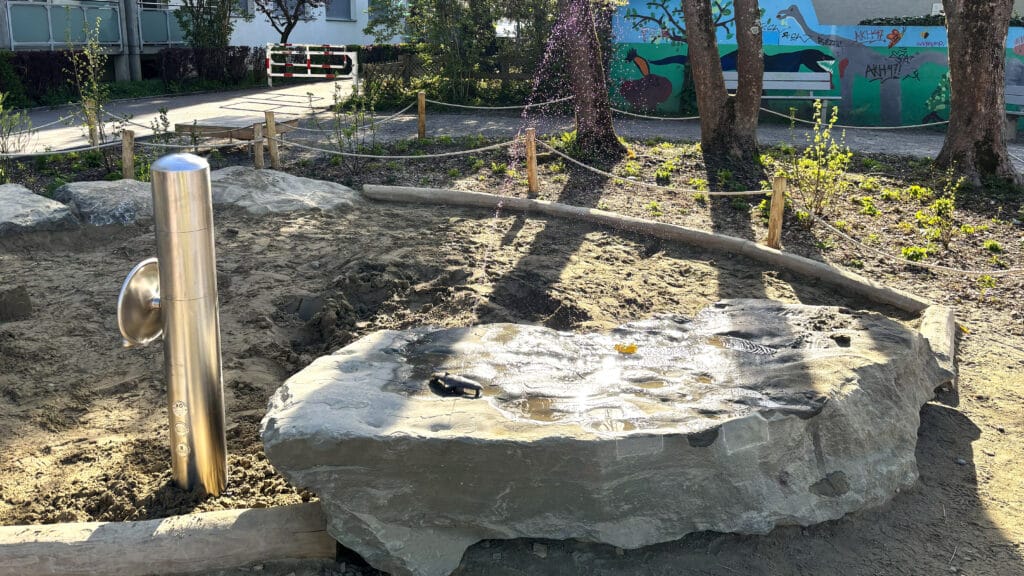Ein neugestalteter Spielplatz mit einem steinernen Wasserbecken und Wasserspiel.