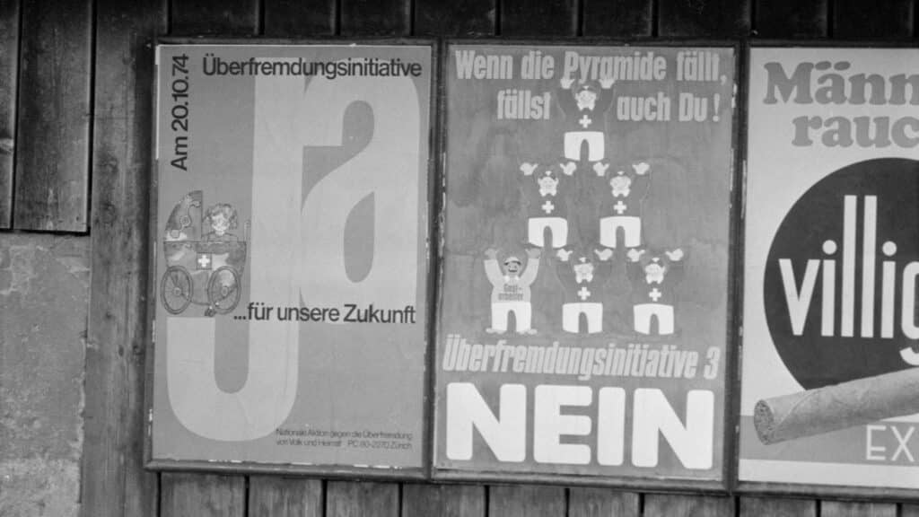Schwarzweissfoto einer Plakatwand mit Abstimmungsplakaten zur Schweizer Überfremdungsinitiative von 1974: links ein "Ja"-Plakat, in der Mitte ein "Nein"-Plakat.