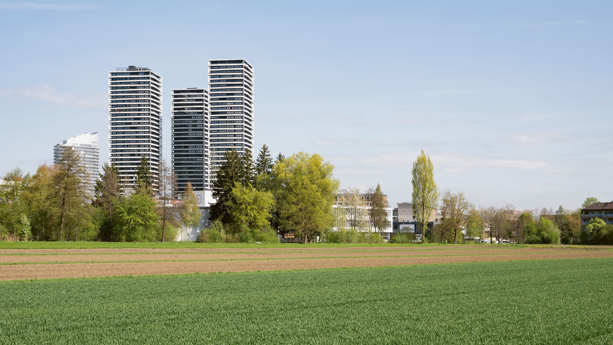 Wohntürme am Rand eines grünen Feldes unter hellem Himmel.
