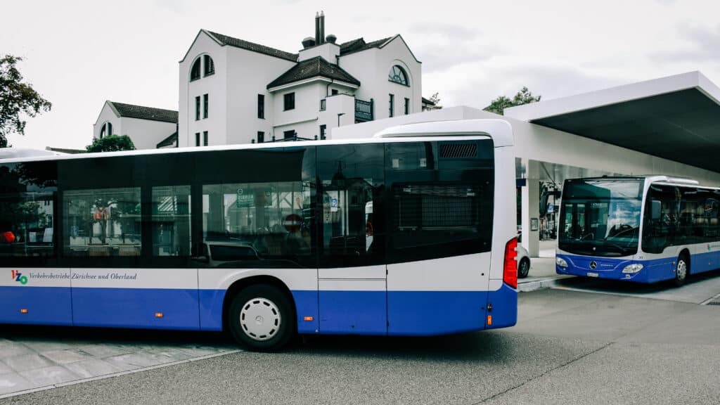 Zwei blau-weisse VZO-Busse an der Haltestelle vor dem Bahnhof Meilen.