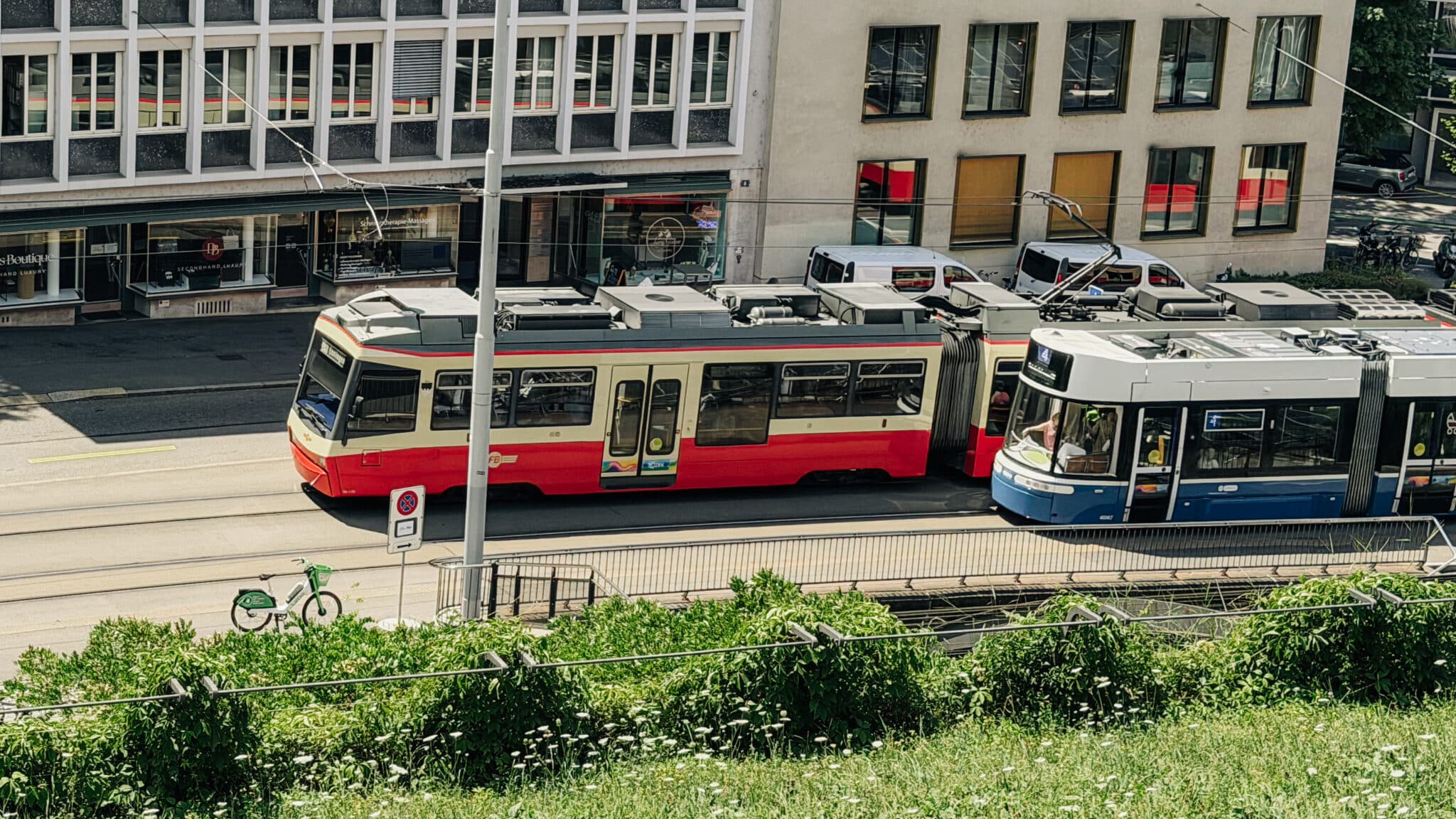 Zwei Trams fahren auf einer sonnigen Stadtstrasse aneinander vorbei.