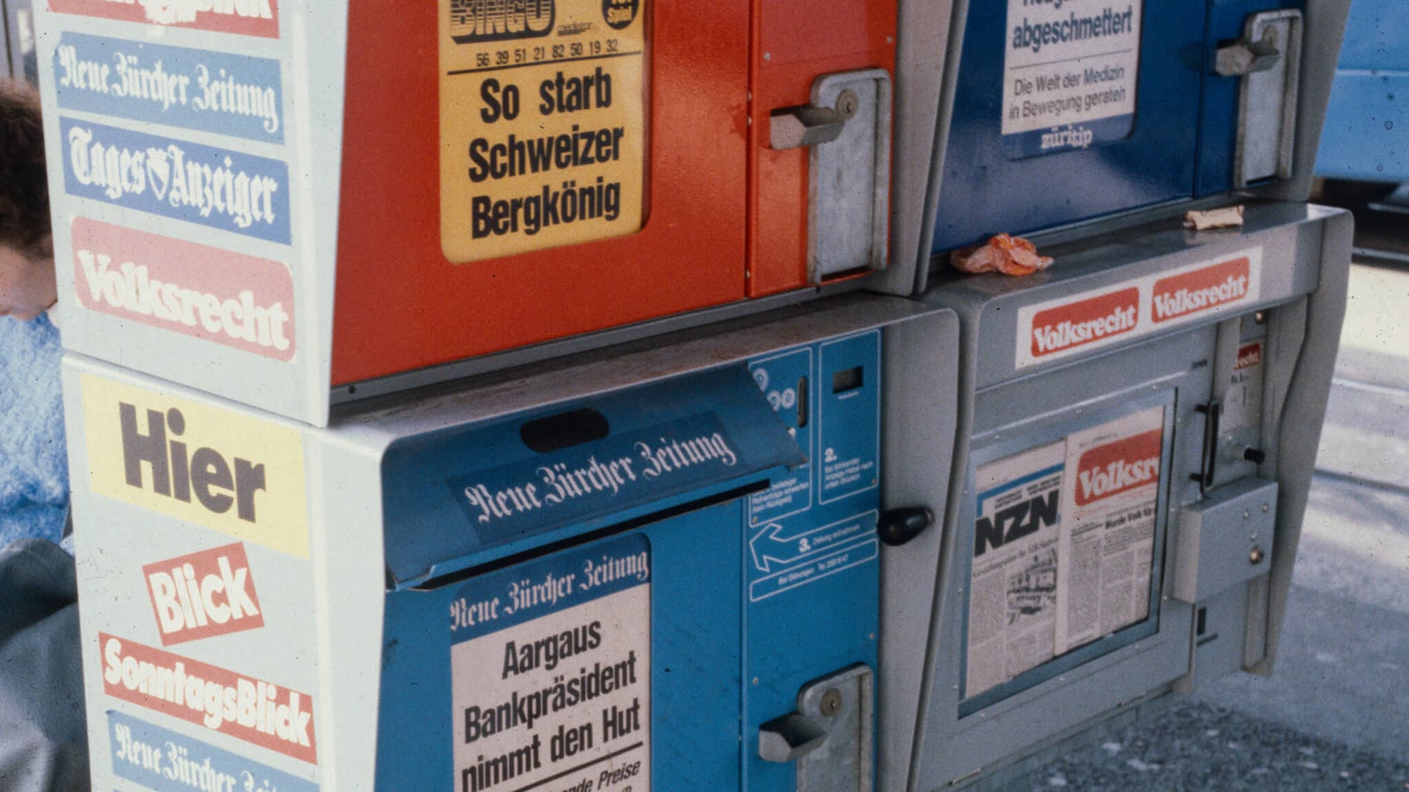 Alte Zeitungsautomaten mit Schweizer Zeitungstiteln und sichtbaren Schlagzeilen.