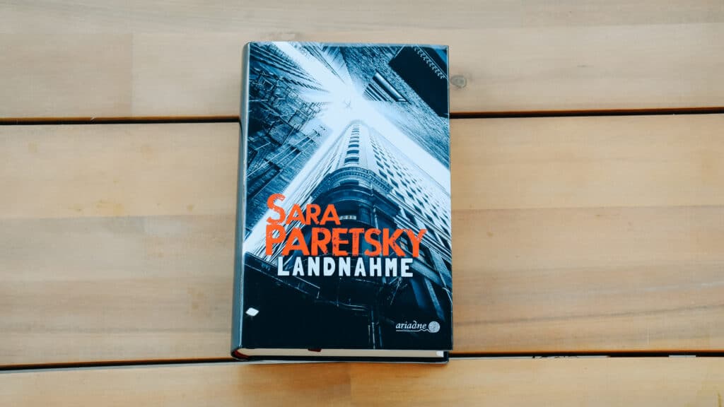 Das Buch "Landnahme" von Sara Paretsky auf einem Holztisch.