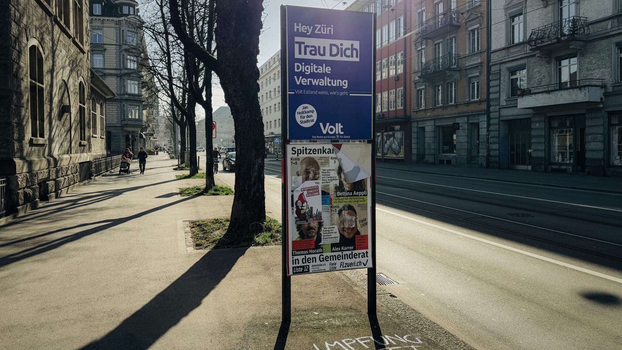 Wahlplakate an einer Zürcher Strasse. Ein grosses Plakat von Volt und mehrere kleinere, zerstörte Kandidierendenplakate der Liste 12 darunter.