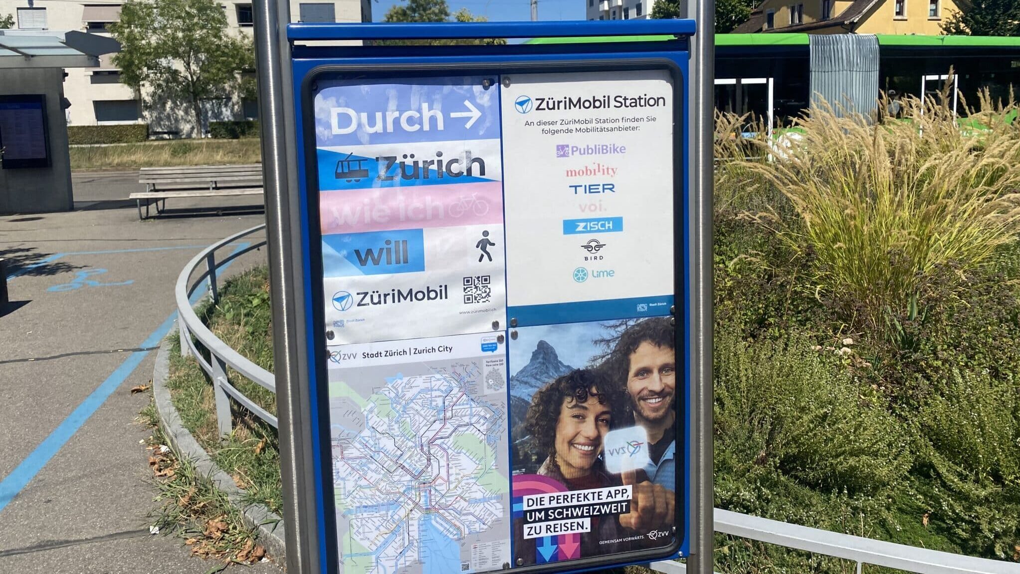 Zu sehen ist ein veralteter Aushang an der VBZ-Tramenstation Seebach. Im Hintergrund hat es eine Sitzbank und Grünpflanzen.