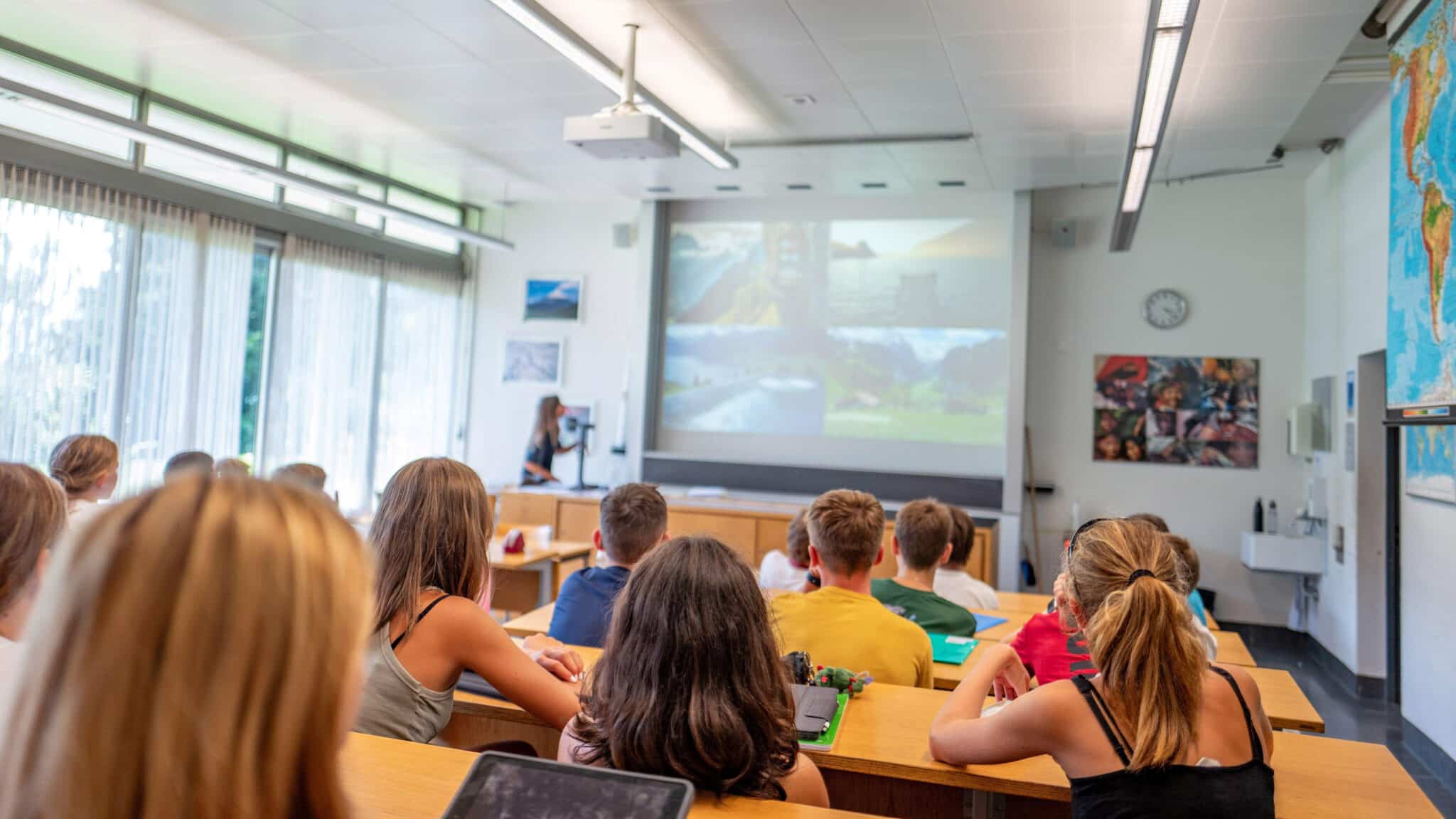 Schulklasse sitzt in einem Klassenzimmer und schaut eine Präsentation auf der Leinwand.