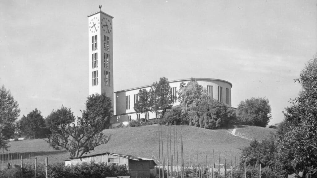 Schwarz-Weiss-Aufnahme einer Kirche mit hohem Uhrturm auf einem Hügel.