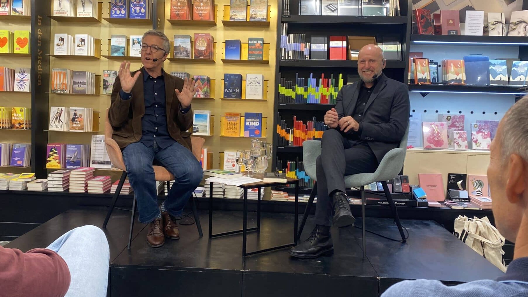Links sitzend mit Brille Thomas Matthys, rechts Autor Andreas russenberger, der lächelnd in de Kamera blickt. im Hintergrund eine Bucherwand. Ort: Der Buchladen Orell Füssli.