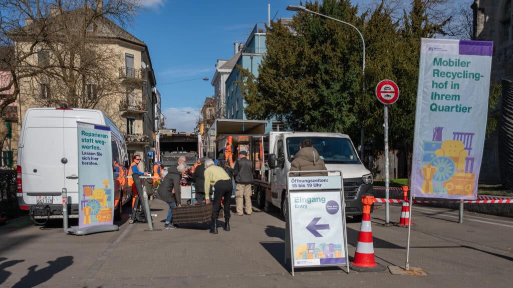 Mobiler Recyclinghof in einer Zürcher Quartierstrasse mit Sammelfahrzeugen, Mitarbeitenden und Menschen bei der Entsorgung.
